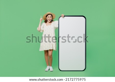 Full body young happy woman she 20s wears white dress hat point finger up big huge blank screen mobile cell phone with workspace copy space mockup area isolated on plain pastel light green background