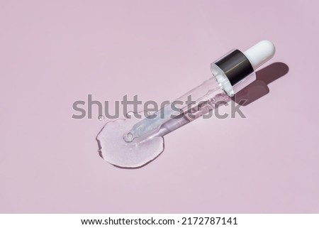 Transparent pipette with blue cosmetics serum on a light pink background. Product texture. Dropper glass bottle branding mockup. Cosmetic pipette