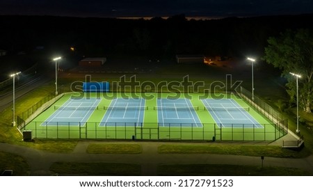 Evening aerial photo of outdoor blue tennis courts with pickleball lines with lights turned on.	 Royalty-Free Stock Photo #2172791523