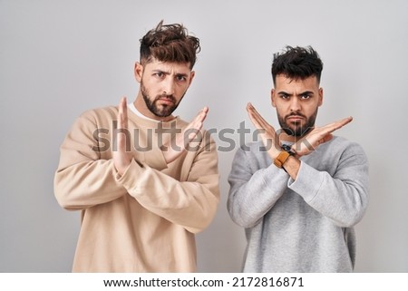 Young homosexual couple standing over white background rejection expression crossing arms doing negative sign, angry face 