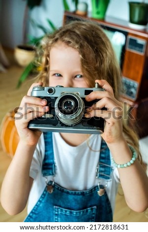 the white teen girl takes pictures on a retro camera and laughs. hobby for kids and happy childhood.