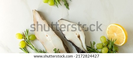 raw halibut steaks, tarragon, lemon and grapes on a light marble table