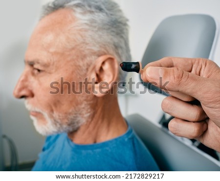 Close-up of intra-ear hearing aid, near senior male patient's ear at audiology clinic. Hearing solutions, hearing aids Royalty-Free Stock Photo #2172829217