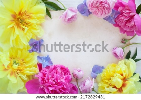 Colorful floral background with pink and yellow peonies, roses, blue hydrangea and paper for holiday greeting text.