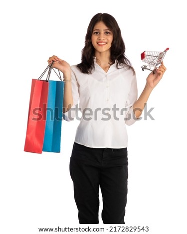 Beautiful young girl holding and posing with a miniature trolley shopping cart and shopping bags on a white background