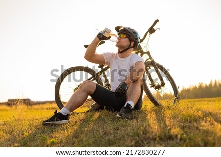 Young professional cyclist dressed in cycling clothing and protective helmet drinking water from the bottle. Active healthy lifestyle. Sports man resting after exercise in nature. Mountain bike. Royalty-Free Stock Photo #2172830277