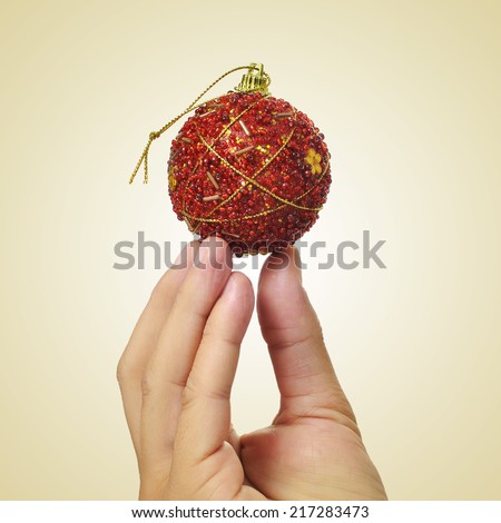 picture of a man hand holding a red christmas ball on a beige background, with a retro effect