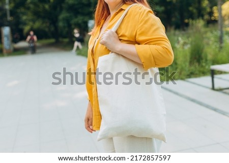 Woman with white cotton shopping bag in her hands in the city street. Mockup and zero waste concept. Eco Nature Friendly Style. Environmental Conservation Recycling mock up. No face