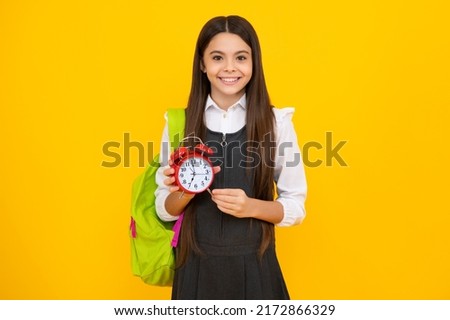 Happy girl face, positive and smiling school girl isolated on yellow. Back to school. Schoolchild, teenage student girl with clock alarm, time to study.