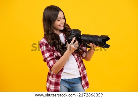Positive and smiling emotions of teenager girl with dslr professional photo camera with big photo lens. Child photographer isoalted on yellow background. Photo school.