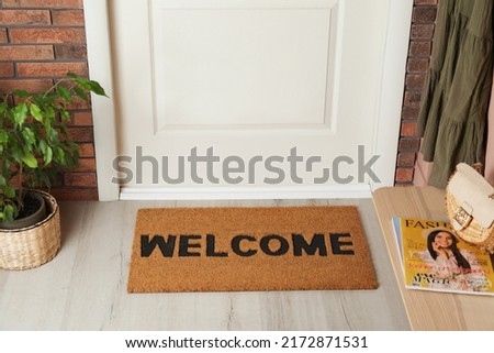 Door mat with word Welcome on wooden floor in hall Royalty-Free Stock Photo #2172871531