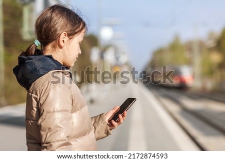 Girl Teen waiting on Railway Station Platform using Mobile Smart phone on blurred background of Train. Online Train Schedule. Paying online Ticket.
