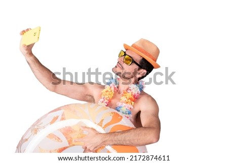 close-up portrait side view of a young male tourist with a flower necklace and hat and sunglasses holding inflatable float posing for a selfie picture.
