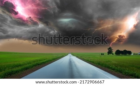 dramatic storm at sunset producing a powerful tornado twisting through the countryside with sheet lightning. Along the road and lightning. powerful lightning bolt strikes the ground in an open field