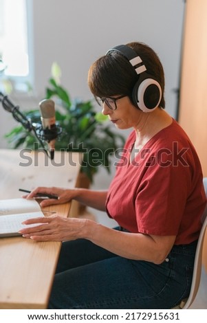 Mature woman making podcast recording for her online show. Attractive business woman using headphones front of microphone for a radio broadcast