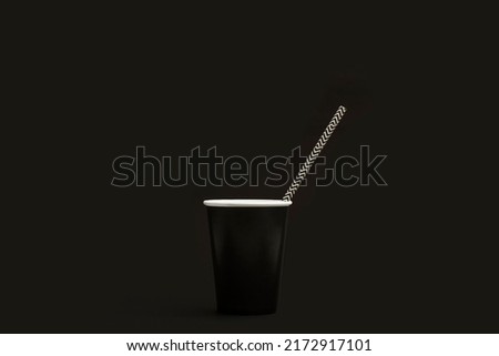 Drinking straw in a black paper drinking glass on a black background with copy space