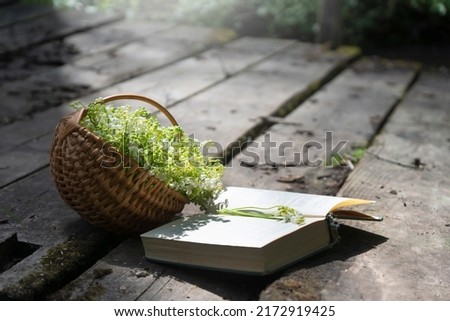A bouquet of lilies of the valley in a basket, a book on the bridge.
