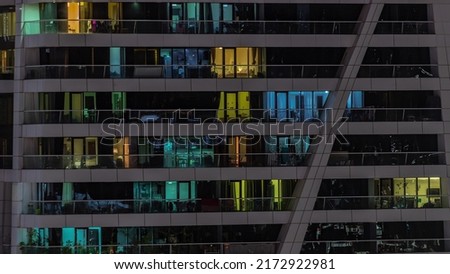 Night view of many glowing panoramic windows in apartment residential tower timelapse. High rise skyscraper with lights in rooms