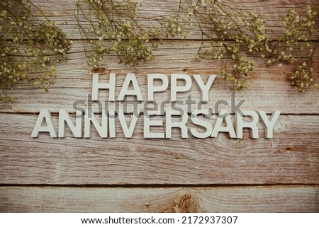 Happy Anniversary alphabet letters with flowers frame on wooden background