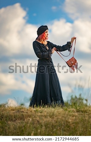 A woman in black looks like a witch against a blue sky with clouds