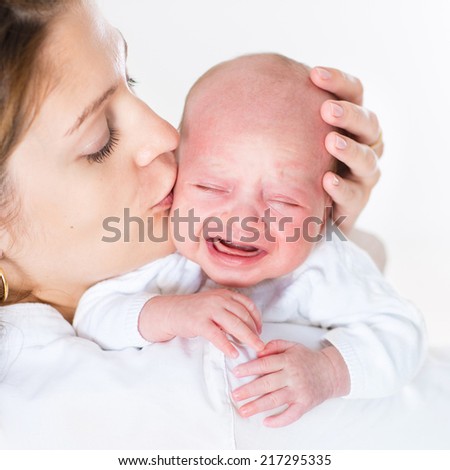 Young mother kissing her crying newborn baby