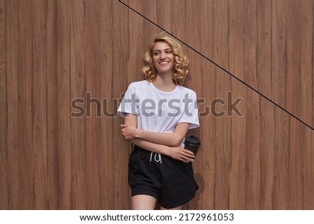 Beautiful smiling girl with blonde hair holding a cup of coffee. Woman on the wooden background. Good morning.
