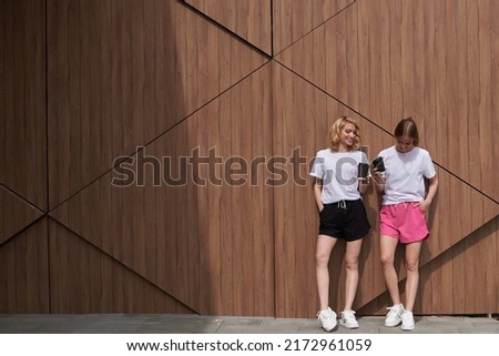 Smiling fitness girls with blonde and dark hair holding a cup of coffee. Teenagers on the wooden background. Good morning. Sport wearing.