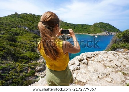 Young hiker explorer girl taking picture with smartphone of natural tropical panoramic view. Wide angle. Windy day.