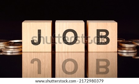 JOB text on wood cubes with coins, black background, business concept. the inscription on the cubes is reflected from the surface of the black table. front view.