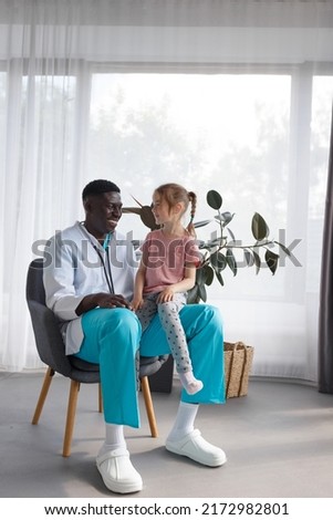 little girl sitting on the lap of an african american doctor Family doctor Royalty-Free Stock Photo #2172982801