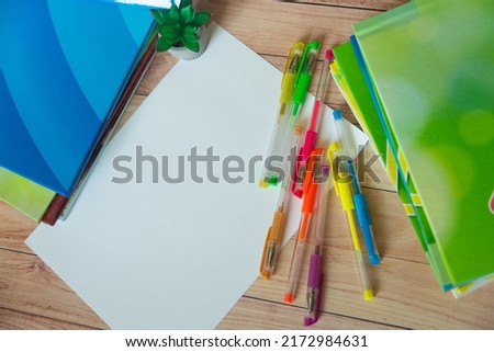 White blank sheet of paper lay on wooden table near colorful books, different pens. Top view, copy space for text. back to school, office stationary