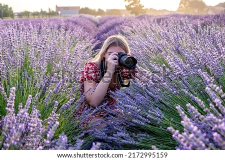 A young beautiful female professional photographer taking pictures in a lavender field on a scenic summer sunrise.