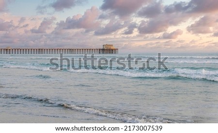 Panorama Puffy clouds at sunset Empty beach with pier and sandy shore at Oceanside in California. Calm ocean waves with a view of a pier against the white sunset sky background. Royalty-Free Stock Photo #2173007539