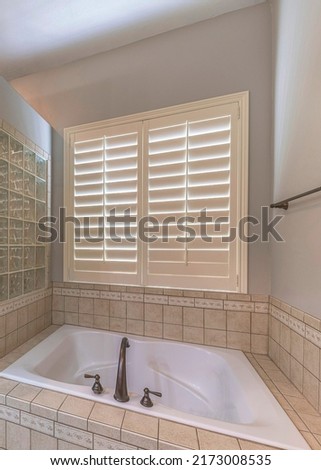 Vertical Bathtub with ceramic tiles surround and glass blocks wall. Bathroom interior with jalousie window on the right near the shower stall with glass door. Royalty-Free Stock Photo #2173008535