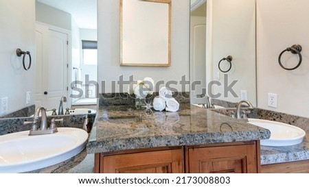 Panorama Double vanity sinks with cabinet countertop and picture frame in the middle. There are two wall mirrors above the sinks with granite top and there are two towel ring holders