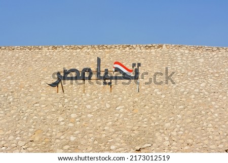 Arabic calligraphy text Tahya Misr (Long live Egypt) with the Egyptian flag on a hill with a blue sky for Egyptian national day 6 October war 1973 and also used for National real estate new projects