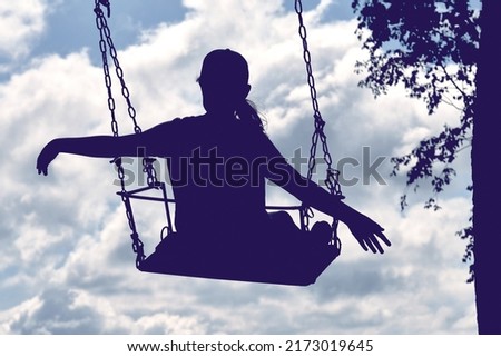 Happy child 10-12 years old swings on a chain swing on a summer day. The swing hangs from the tree, the girl flies on the seesaw in the clouds.