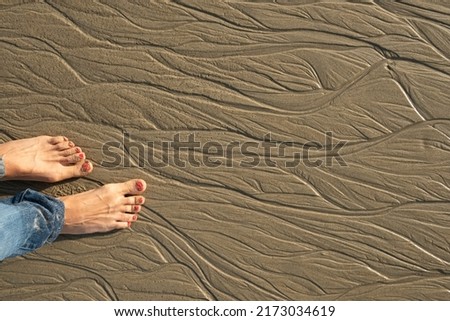 Bare feet in the sand on the beach sand. Patterns on the sand from the water at low tide. Royalty-Free Stock Photo #2173034619