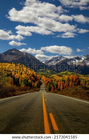 Sunny autumn afternoon scenic drive in the San Juan Mountains near Telluride Colorado along the San Juan Skyway Scenic Byway with snow covered peaks in distance with yellow and orange Aspen trees Royalty-Free Stock Photo #2173041585