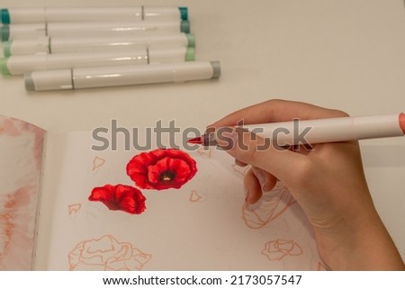 Hand drawing a red poppy wreath sketch in a sketchbook with alcohol based sketch drawing markers. Remembrance Day and Anzac day. Royalty-Free Stock Photo #2173057547