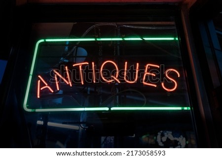Red and green antiques sign glowing from a dark window