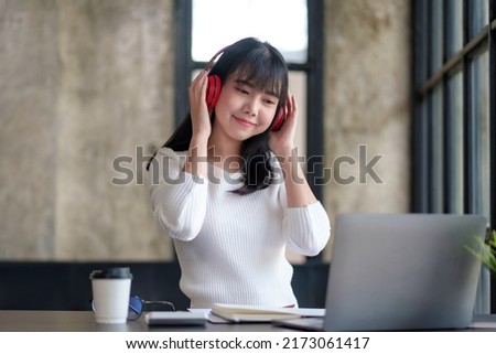 Cute Asian woman wearing headphones sitting listening to music happily enjoy listening to music at home.