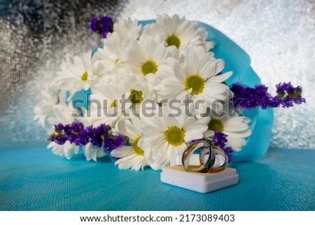 Wedding bouquet of bride. wedding card with original rings in a white box, a bouquet of white chrysanthemums or daisies and a white lace fan on a blue background