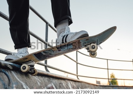 Photo of sports guy skateboarder at skate park with graffiti walls posing on skateboard.