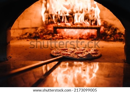 The chef puts the Margherita, four cheese or meat pizza on a shovel in the oven. A firewood oven for cooking and baking pizza. Italian traditional pizza is cooked in a stone wood-fired oven.