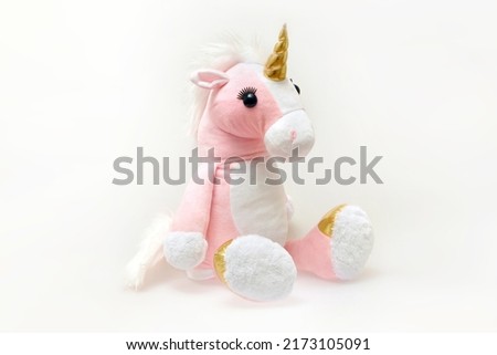 Image of a pink soft unicorn toy sitting at white background. Isolated studio image