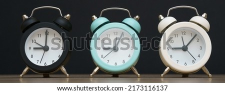 Three small alarm clocks black blue and white show nine o'clock, stand on a table on a black background