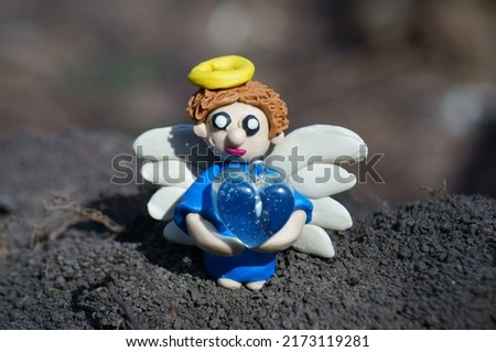 A toy angel made of plasticine with a heart in his hands. A symbol of hope, happiness and well-being.