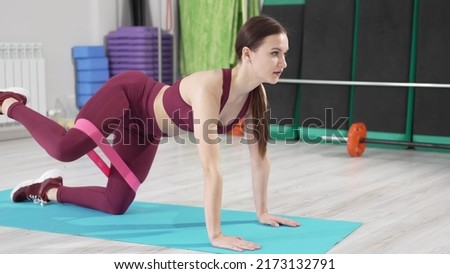 a young woman in a burgundy tracksuit does elevation legs with gymnastic elastic bands on a mat. video and online lessons for sports. clothes and shoes for gymnastics. professional fitness trainer.