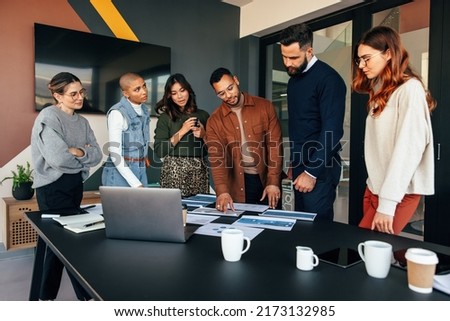 Team of businesspeople discussing some documents in a boardroom. Group of multicultural businesspeople standing around a table in a modern office. Diverse entrepreneurs collaborating on a new project. Royalty-Free Stock Photo #2173132985